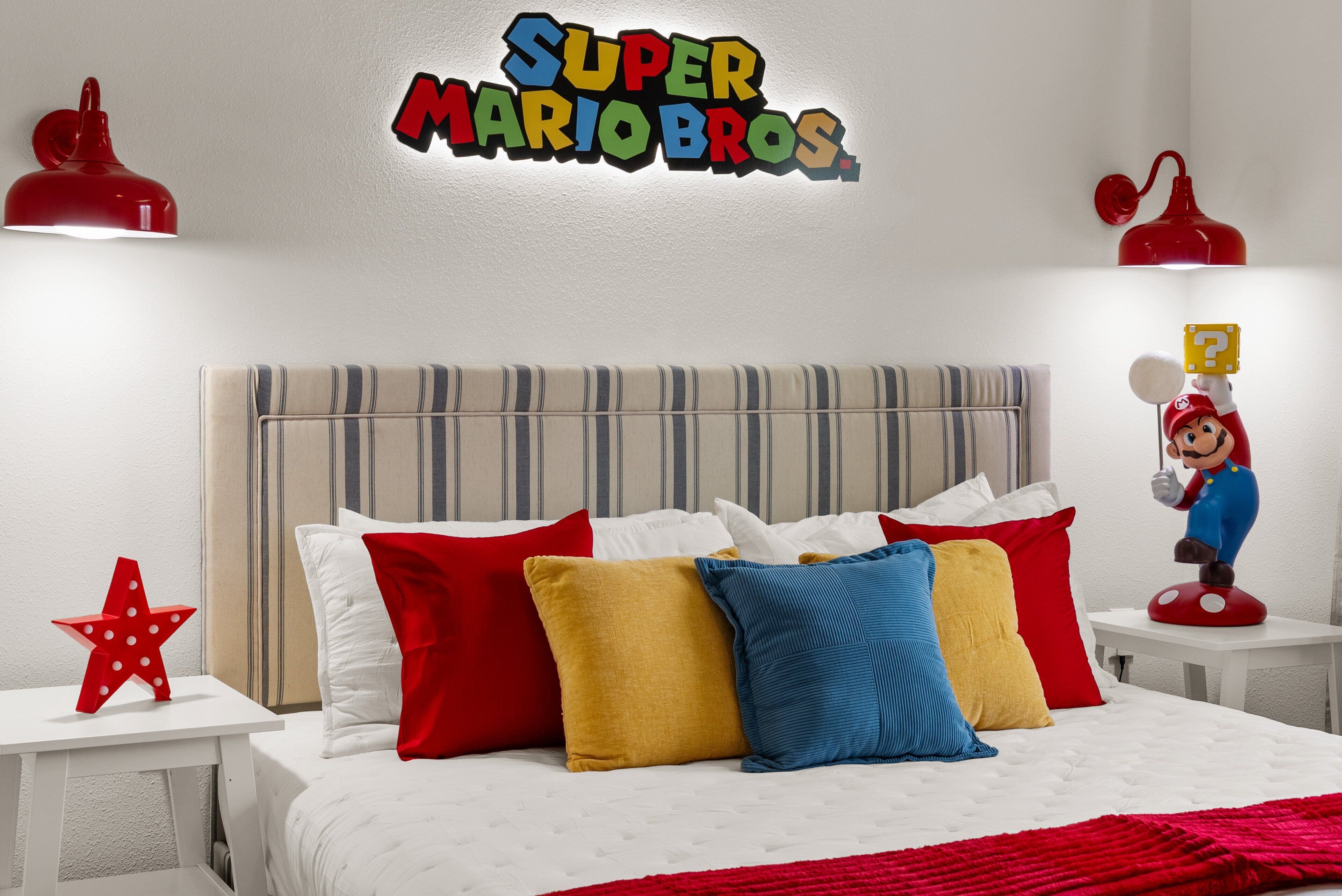 A bedroom with a bed, pillows, a Mario figurine, and a wall sign.