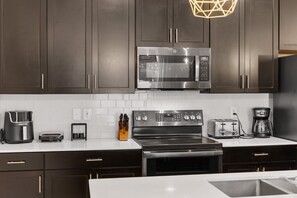 Une cuisine moderne avec des meubles de couleur sombre, des appareils en acier inoxydable et un plan de travail blanc.