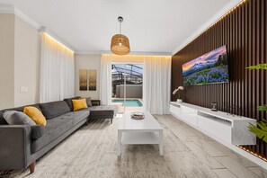 Un salon moderne avec un canapé gris, une table basse blanche et un grand téléviseur fixé sur un mur en bois.