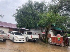 A parking area with two white pickup trucks and a white car. There is a building with a red roof and a signboard. - Manowwhan Homestay (Kaeng Krachan)