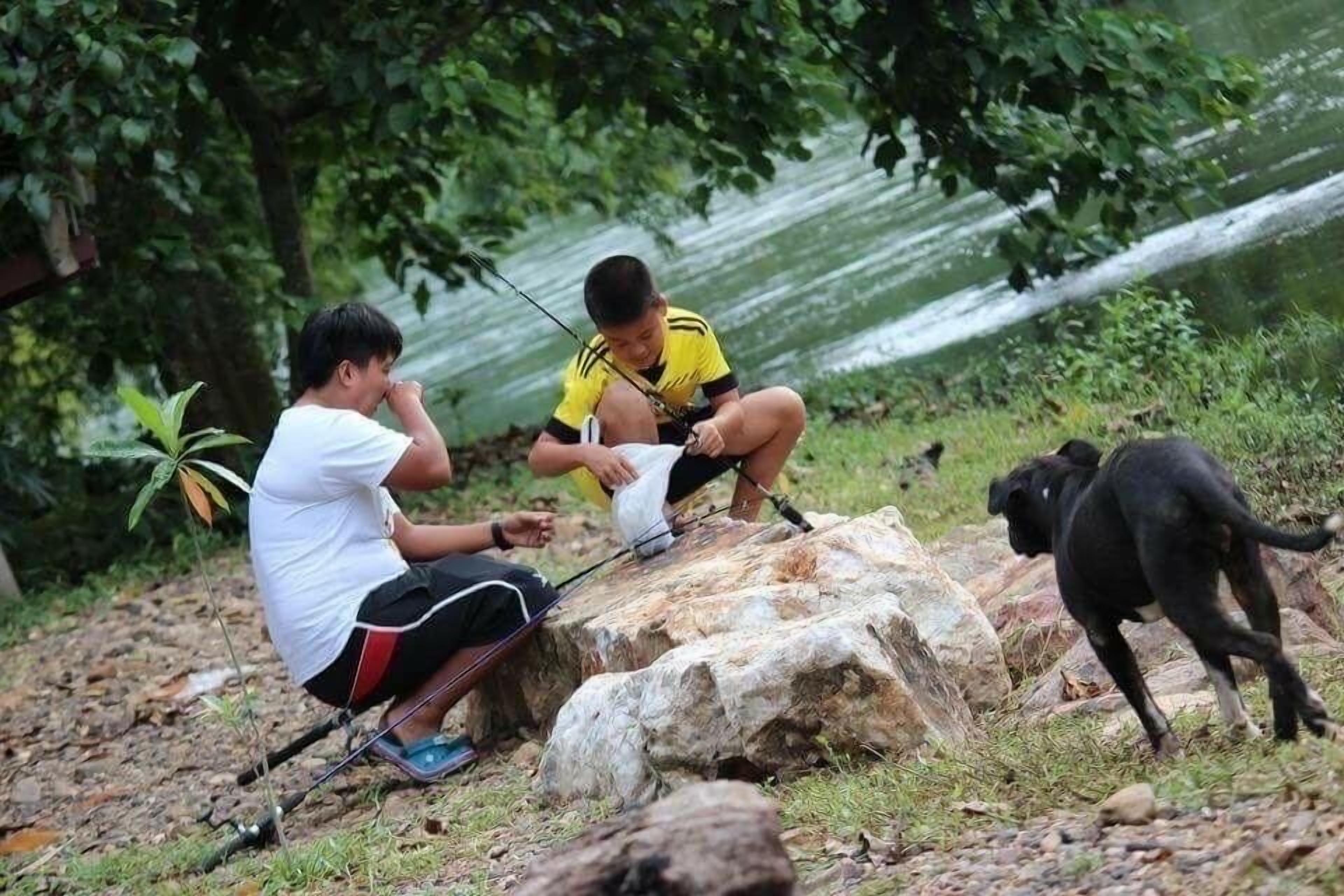 Two people fishing by a river with a dog nearby.