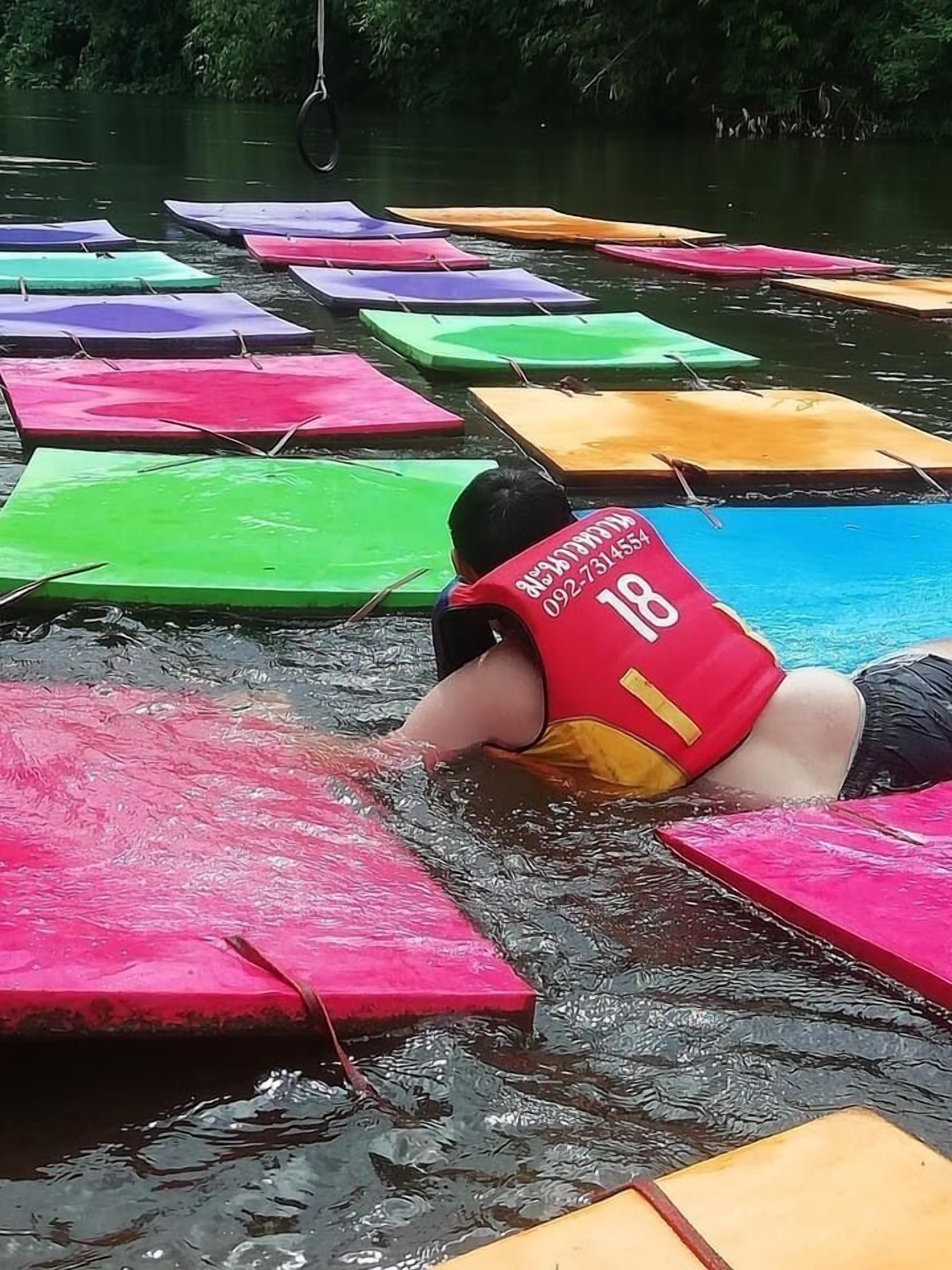 A person in a red life jacket floating on a water body with colorful floating platforms.
