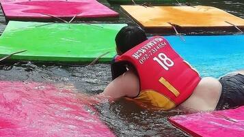 A person in a red life jacket floating on a water body with colorful floating platforms.