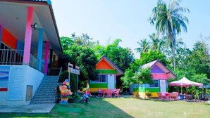 Un edificio colorido con una escalera que conduce a un área cubierta, rodeado de exuberante vegetación y palmeras.