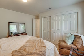 Een slaapkamer met een bed, een stoel, een dressoir, een spiegel en een kast.