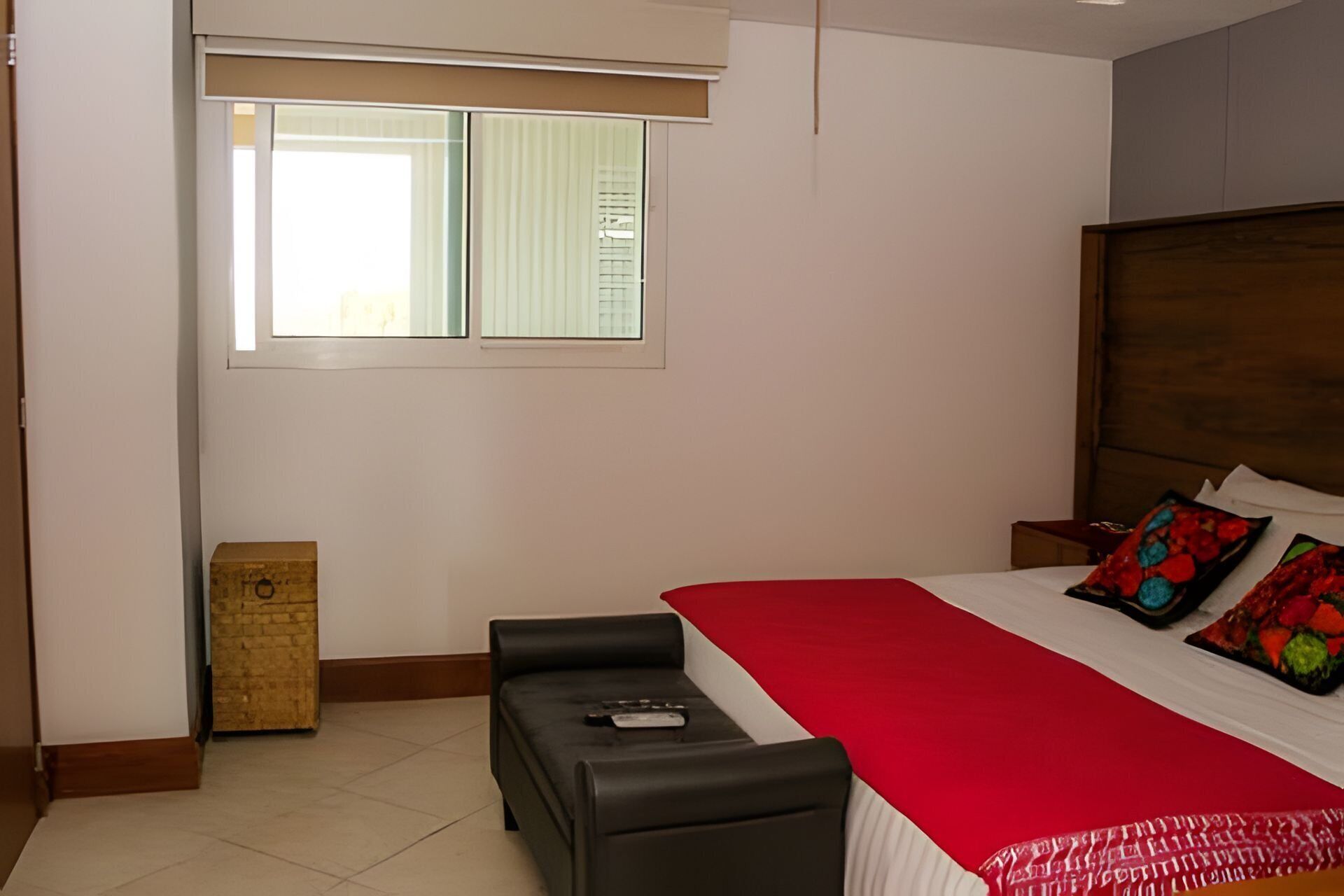 Un dormitorio con cama, una banca, una ventana y un armario de madera.