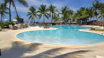 A large, clear swimming pool surrounded by lounge chairs and palm trees.