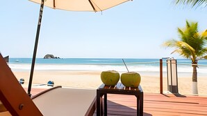 A beach view with a wooden deck, two coconuts on a table, and a beach umbrella. - 302 S Bay View Grand Residencial Ixtapa (Ixtapa)