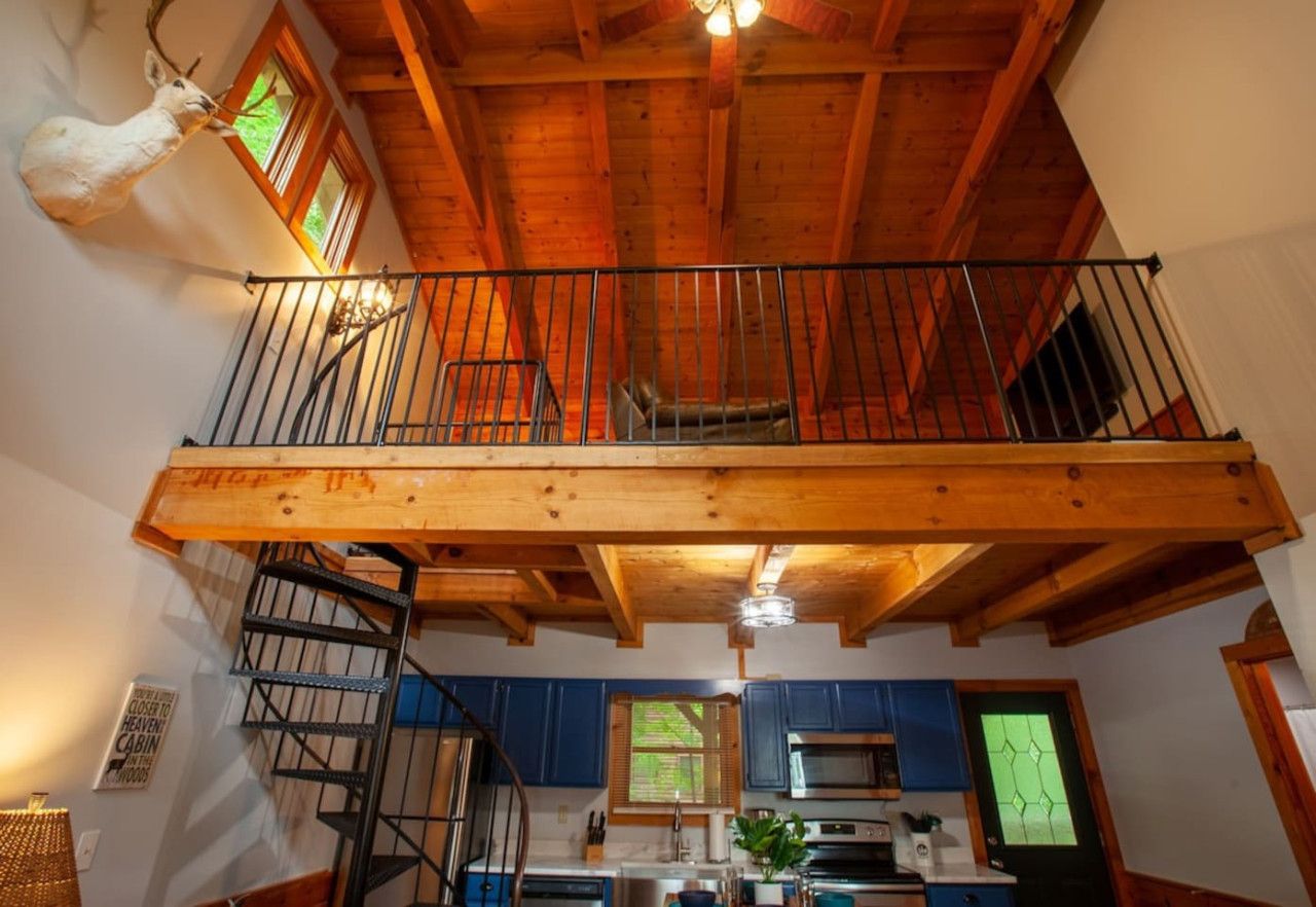 A cabin interior with a wooden balcony, a spiral staircase, and a mounted animal head.