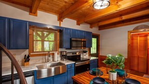 A kitchen with blue cabinets, a stainless steel sink, and a wooden dining table with blue plates.