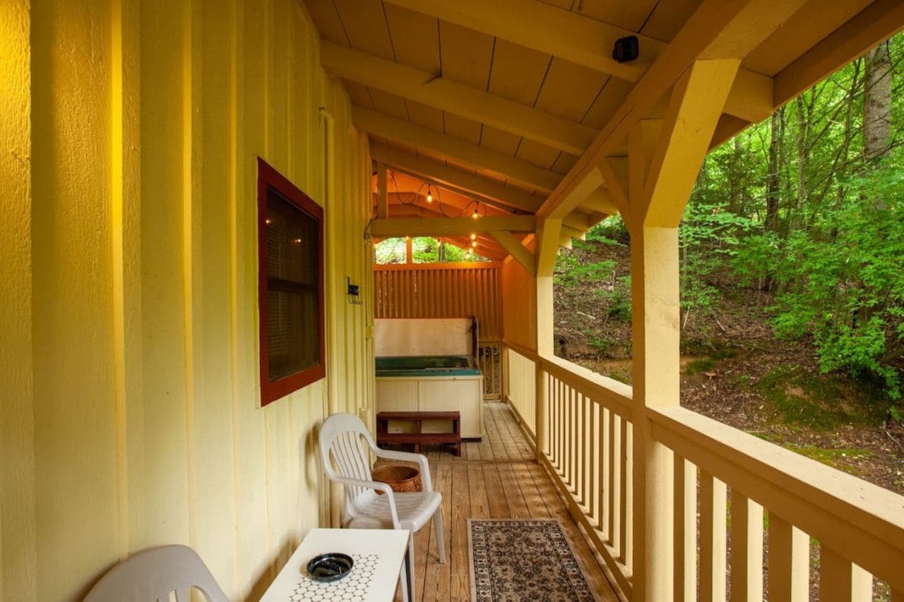 Eine überdachte Veranda mit Tisch und Stühlen, einer Bank und Blick auf einen Wald.