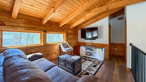 A cozy log cabin interior with a wooden ceiling, a sofa, a chair, a television, and a small cabinet.