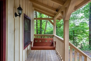 A wooden porch with a bench, a window, and a view of a forest.