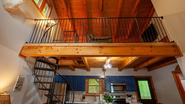 A rustic cabin interior with a wooden balcony, a spiral staircase, and a mounted animal head.