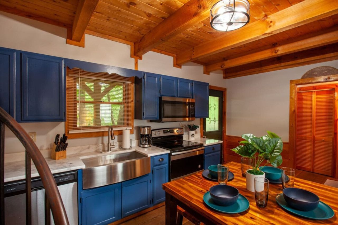 A kitchen with blue cabinets, stainless steel appliances, and a wooden dining table set for four.