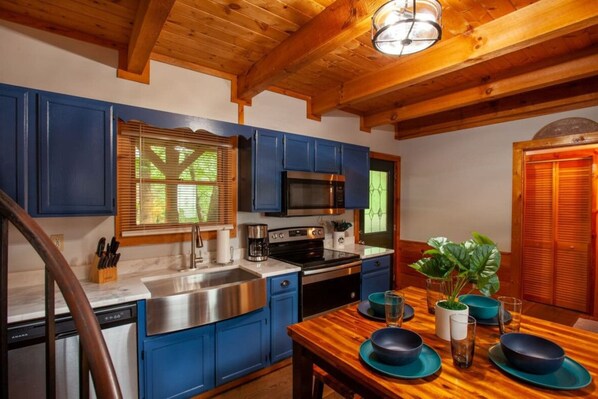 A kitchen with blue cabinets, stainless steel appliances, and a wooden dining table set for four.