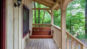 A wooden porch with a bench, a window, and a view of a forest.