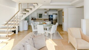 Ein modernes Wohnzimmer mit Treppe, einem Essbereich mit Glastisch und einer Küche im Hintergrund.
