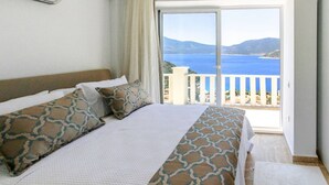 Ein Hotelzimmer mit Bett, Kissen und Meerblick vom Balkon aus.