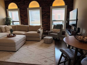 A living room with a sectional sofa, a small armchair, a wooden coffee table, a side table, and a television.