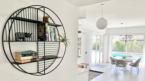 Una sala de estar moderna con una estantería circular de metal negro, una mesita de madera y un comedor con vista a la piscina.