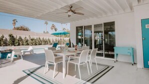 Un patio techado al aire libre con piscina, muebles blancos y un mueble de color aguamarina.