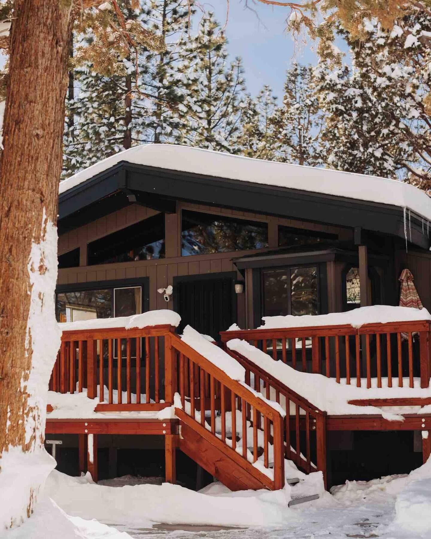 A two-story building with a wooden deck and stairs leading to the entrance, surrounded by snow-covered trees.