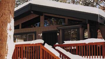 A two-story building with a wooden deck and stairs leading to the entrance, surrounded by snow-covered trees.