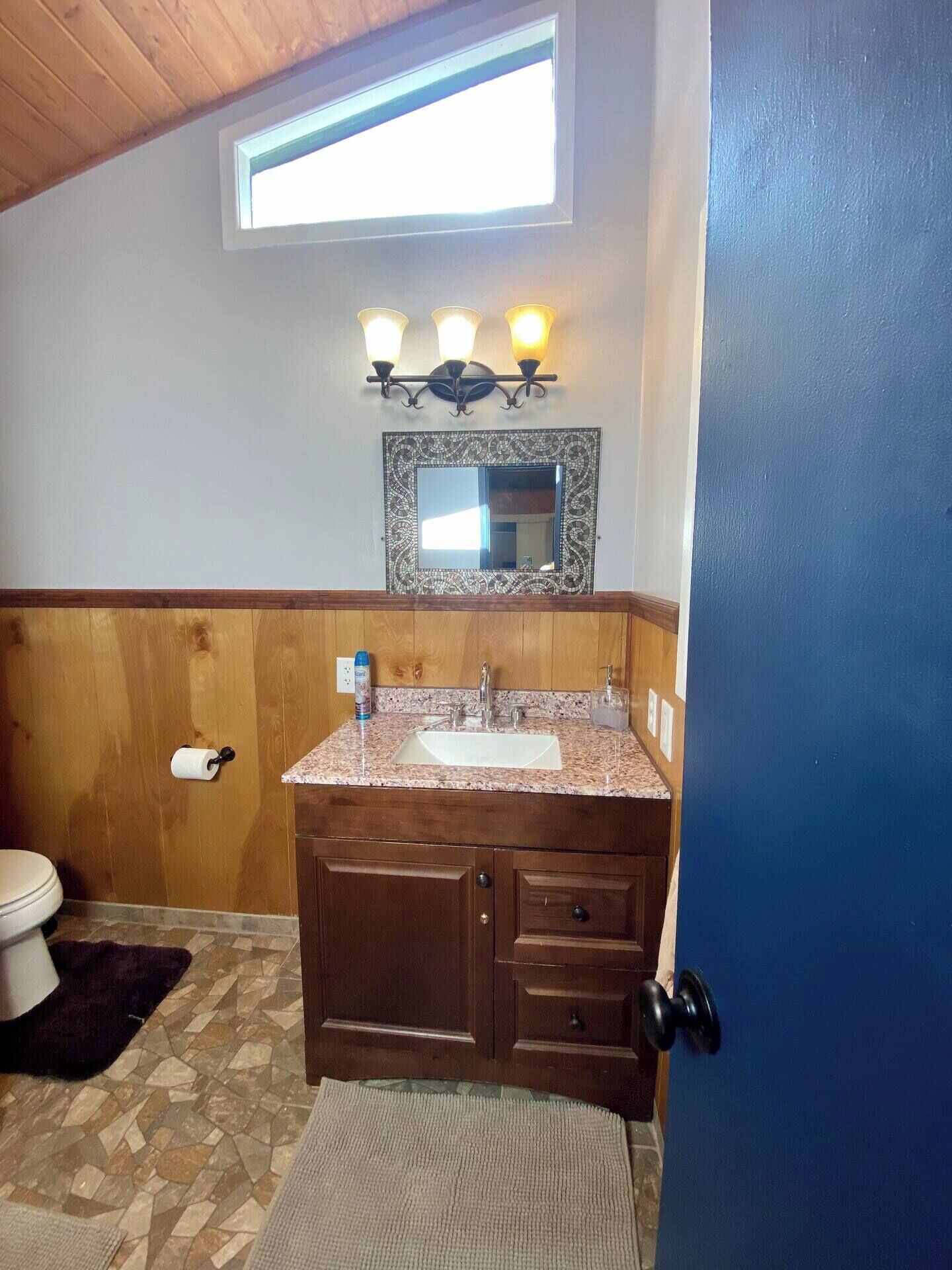 A bathroom with a wooden vanity, a sink, a mirror with a decorative frame, and a window above the vanity.