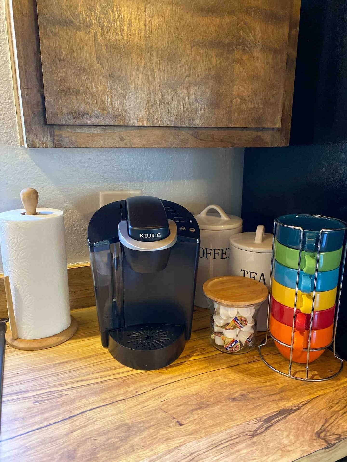 Una cafetera, una caja de bolsitas de té y una taza colorida sobre una superficie de madera.