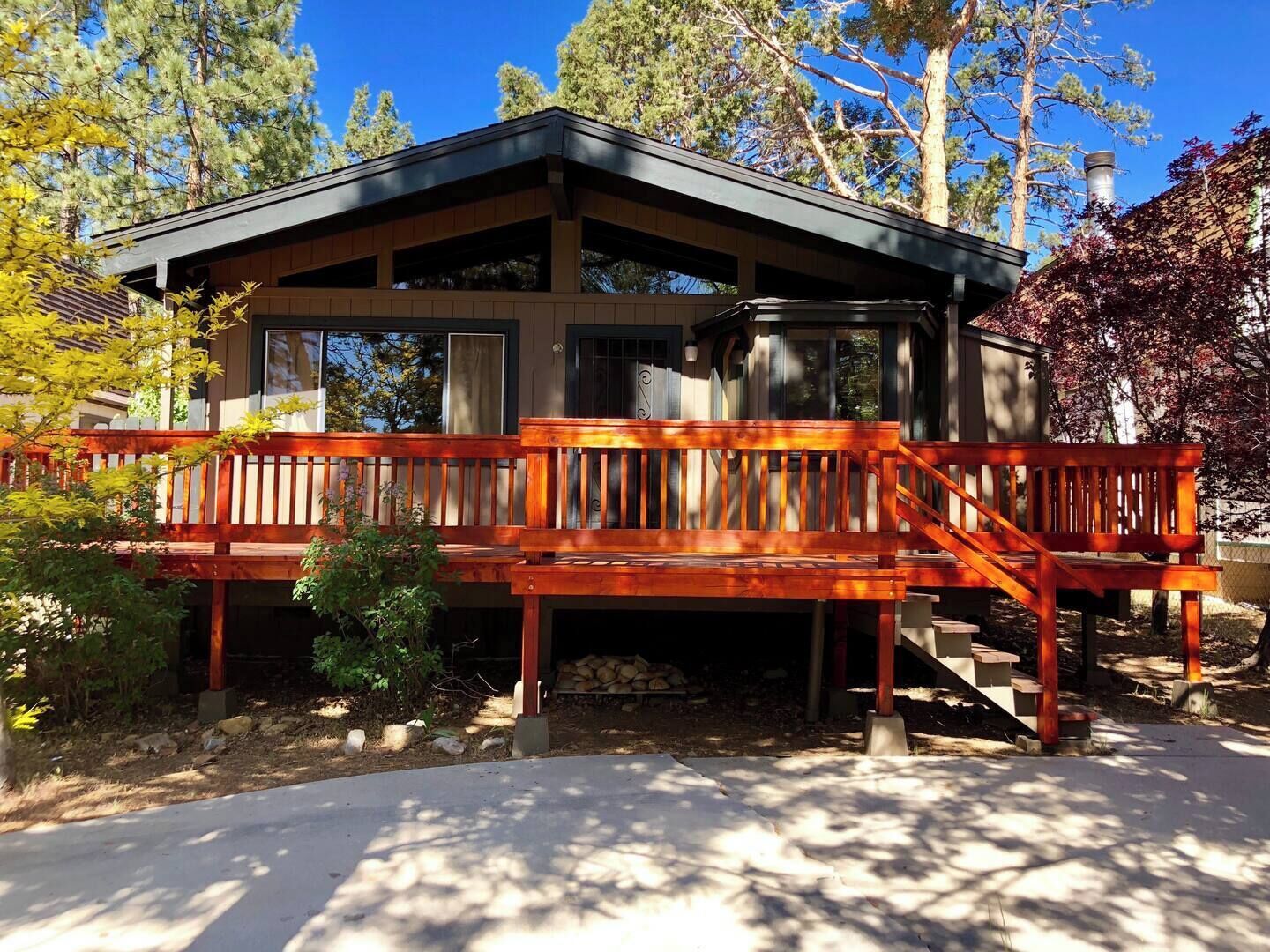 A cabin with a wooden deck, a covered porch, and a stone fireplace.