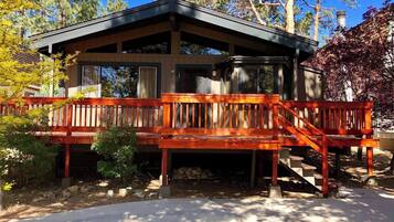 A cabin with a wooden deck, a covered porch, and a stone fireplace.