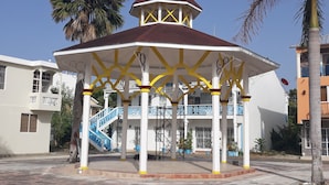 A gazebo with a red roof and yellow accents, surrounded by palm trees and a building with a blue staircase. - MY RELAX- VAMAR LUXURY CONDO (Puerto Plata)