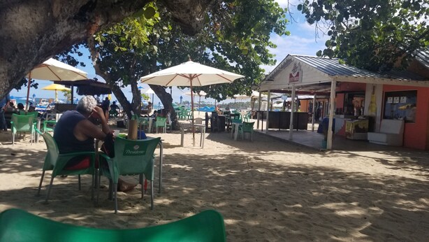 A beachside café with outdoor seating under umbrellas, a small shop, and a sandy beach area. - MY RELAX- VAMAR LUXURY CONDO (Puerto Plata)