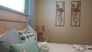 A bedroom with a wooden headboard, a bed with patterned pillows, a bedside lamp, and two wall-mounted artworks of flamingos. - MY RELAX- VAMAR LUXURY CONDO (Puerto Plata)