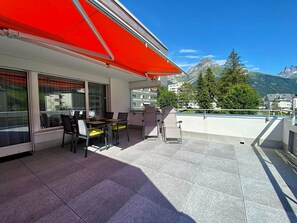 A balcony with a red awning, outdoor seating, and a view of mountains. - Sunnmatt West Wohnung 936 Appartement/Fewo 4-Bettwohnung by Interhome (Engelberg)