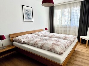 A bedroom with a wooden bed frame, a bedside table with a lamp, a framed picture on the wall, and a window with curtains. - Sunnmatt West Wohnung 936 Appartement/Fewo 4-Bettwohnung by Interhome (Engelberg)