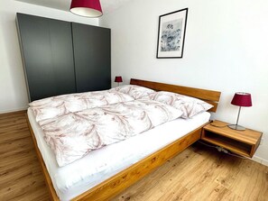 A modern bedroom with a wooden bed, a grey wardrobe, a bedside table with a lamp, and a framed artwork on the wall. - Sunnmatt West Wohnung 936 Appartement/Fewo 4-Bettwohnung by Interhome (Engelberg)