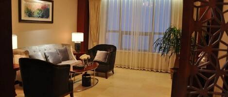 A hotel room with a large window, a sofa, a chair, a coffee table, and a lamp.