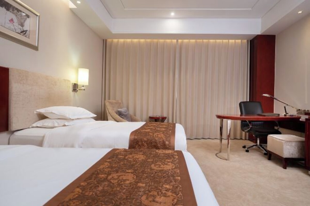 Une chambre d’hôtel avec deux lits, un bureau, une chaise et une grande fenêtre avec des rideaux.
