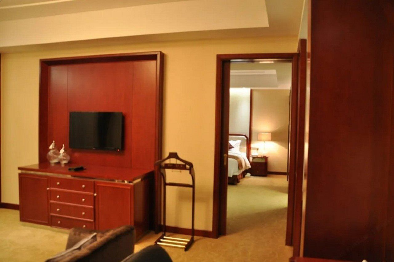 A hotel room with a TV mounted on a wooden cabinet, a bed with a nightstand, and a mirror in the adjacent room.