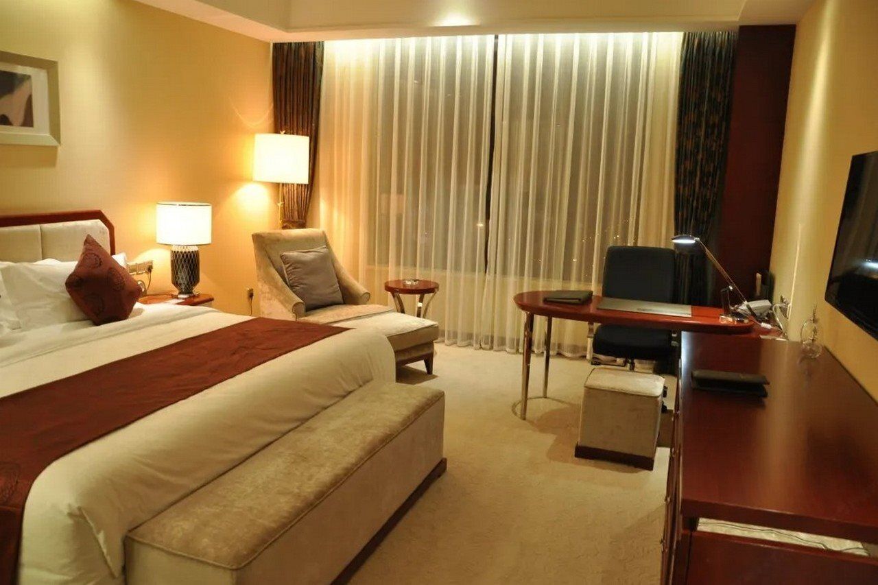 A hotel room with a large bed, a desk, a chair, a TV, and a window with curtains.