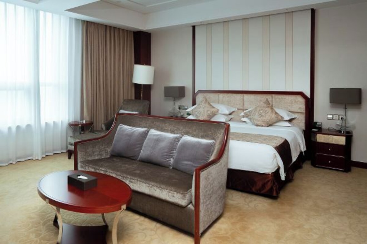 Une chambre d’hôtel avec un lit, un canapé, une table de chevet, une lampe et une vue sur l’extérieur.