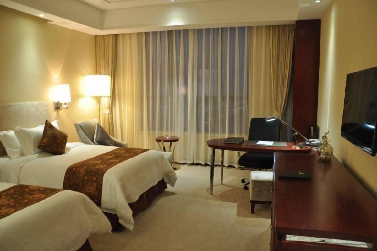 Habitació d'hotel amb dos llits, un escriptori, una cadira, un televisor i una finestra amb cortines.