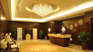 Un hall d’hôtel avec un comptoir d’accueil, un lustre et une moquette à motifs.