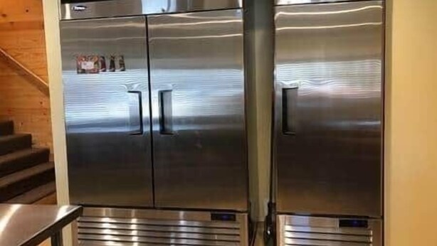 Un réfrigérateur à double porte en acier inoxydable doté d’un écran numérique, situé dans une cuisine au plancher en bois et où l’on peut voir un escalier.