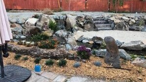 Un jardin avec un sentier en pierre, des rochers et un petit étang.