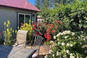 A patio with a table and chairs, surrounded by a garden with various plants and flowers.