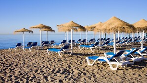 A beach with rows of sun loungers and thatched umbrellas.