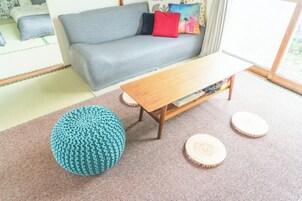 Una sala de estar con un sofá gris, una mesa de centro de madera, un taburete tejido color verde azulado y posavasos redondos de madera sobre la alfombra.